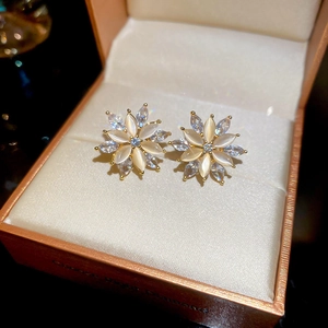 Macro shot of gold flower stud earrings with white cat-eye stones and zircons