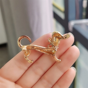 Close-up of golden dachshund dog brooch held by hand showing detailed metal texture