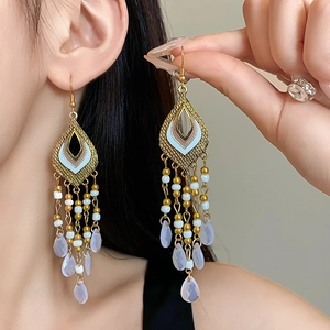 Detail of ethnic gold tassel earrings with intricate beadwork and waterdrop pendants