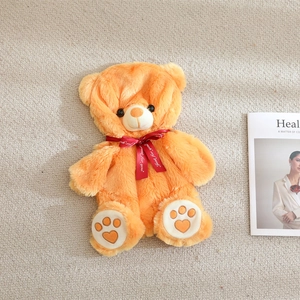 Close-up of orange plush teddy bear showing heart embroidery on paws and silk bow tie