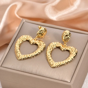 Detailed close-up of hollow gold heart earrings with textured surface on silk fabric