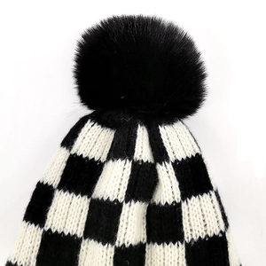 Detail of checkered knit beanie with large black faux fur pompom and thick woven texture