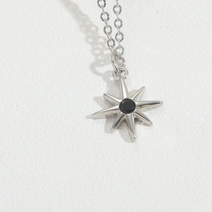 Macro shot of silver eight-pointed star pendant with black gemstone on white leather