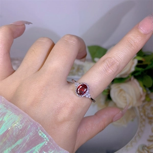 Macro shot of silver ring featuring oval red gemstone surrounded by sparkling zircons