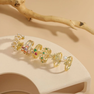 Detailed view of 14K gold-plated rings with zircon and pearls on a beige stand