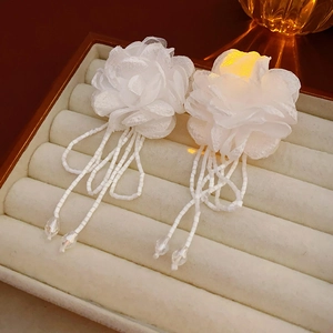 Detailed macro of white fabric flower earrings with elegant beaded tassel on velvet