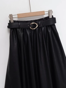Detail of black faux leather skirt texture featuring elastic waist and golden buckle belt