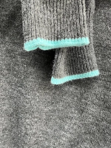 Detail of grey knit sweater cuff with ribbed texture and mint green contrast piping
