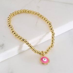 Gold beaded stretch bracelet featuring a pink enamel evil eye charm on marble stand