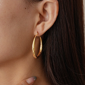 Close-up of golden geometric rhombic textured hoop earring worn on model ear