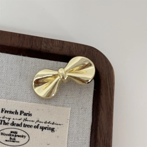 Macro detail of a polished gold bow hair clip on a vintage linen and wood jewelry tray