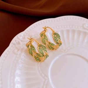 Close-up of golden twist hoop earrings with sparkling green zircon inlays on ceramic
