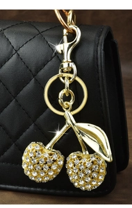 Close-up of sparkling cherry keychain with crystals on a black quilted leather bag