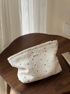 Detail of white woven fabric pouch with colorful polka dots and a black zipper closure