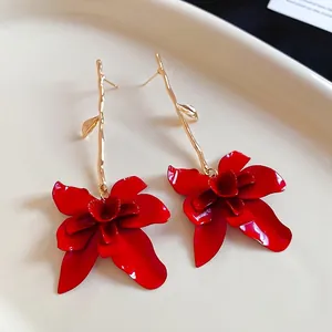Exaggerated red floral drop earrings with gold branch hooks on a ceramic tray