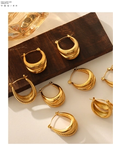 Macro detail of U-shaped gold earrings with unique twisted wavy texture on wood