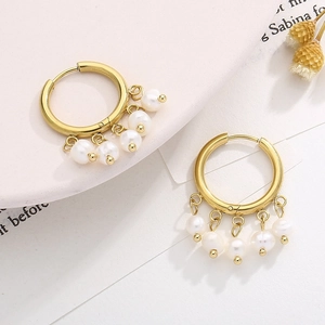 Detail of gold titanium hoop earrings with multiple hanging white pearls on a stone surface