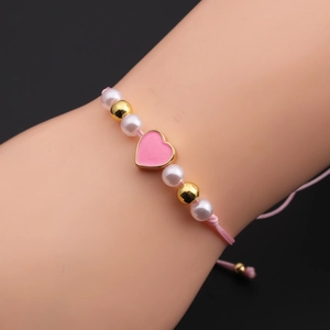 Detail of pink enamel heart charm and white pearls on an adjustable cord bracelet