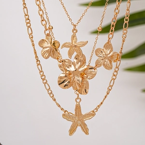 Close-up of layered gold necklace with wrinkled starfish and metallic flower pendants