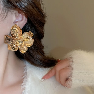 Macro detail of large gold-finish wrinkled flower earrings with metallic textures