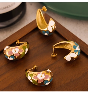 Detailed close-up of C-shaped gold-plated enamel flower earrings on a rustic tray