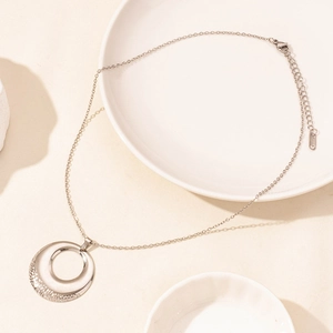 Detail of silver stainless steel necklace with hollow round pendant on white ceramic plate