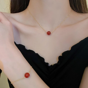 Detail einer vergoldeten feinen Kette und Armband mit roten runden Perlenanhängern