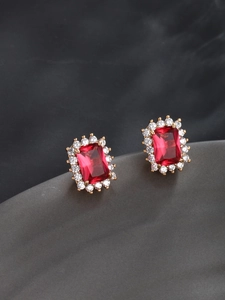 Detailed macro view of gold-plated stud earrings featuring emerald-cut red stone and zircons