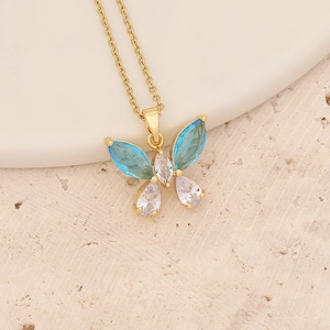Close-up of golden butterfly pendant with blue and white stones on textured stone