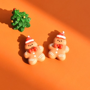 Macro detail of two gingerbread man resin accessories with red hats on orange backdrop