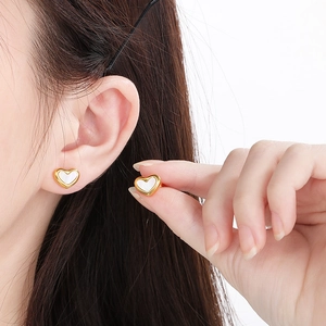 Dettaglio di orecchini a cuore in oro con inserto in conchiglia bianca su modella