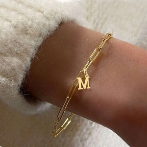 Detail shot of golden paperclip chain bracelet with a custom letter M pendant