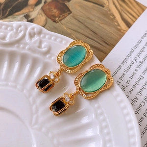 Detail of vintage gold leaf earrings with green gems on a decorative white plate