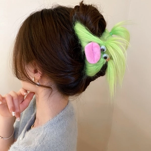 Detail view of a fuzzy green monster hair claw clip with large eyes worn on brunette hair