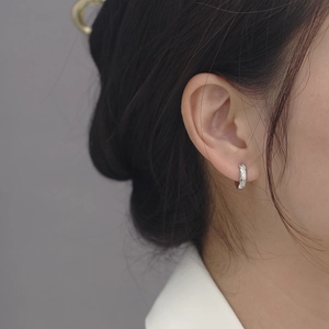 Close-up of silver geometric diamond-pattern hoop earrings worn by a model