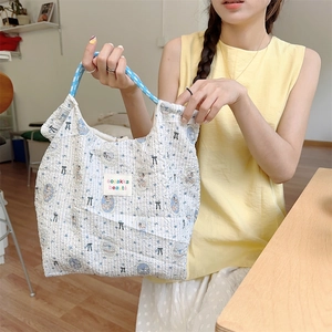 Quilted tote bag with bear pattern and blue woven handles shown held by a person