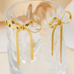 Detailed shot of golden bow earrings with snake chain tassels on a textured glass rim