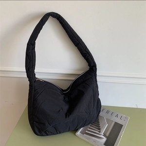 Detail view of black quilted puffer tote bag on a light green table with a magazine