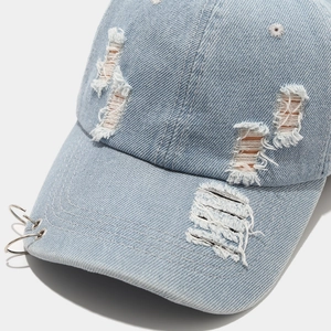 Close-up of distressed light blue denim baseball cap with torn details and three silver rings