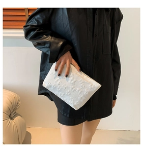 Detailed view of white clutch bag featuring elegant 3D floral embossing and high-quality texture
