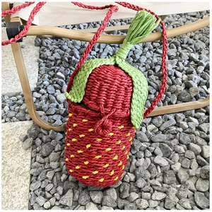 Detailed view of strawberry-shaped straw woven crossbody bag with green leaf top