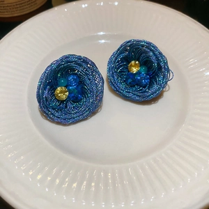 Close-up of blue woven wire flower earrings with crystals on white ceramic plate