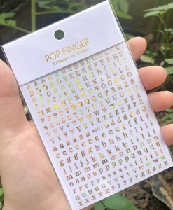 Close-up of WG719 golden 3D English letter nail stickers with various font sizes