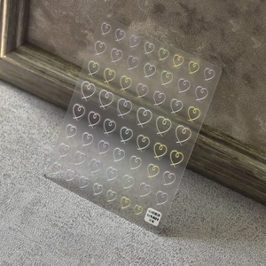 3D embossed heart nail stickers with metallic gold and pink colors on textured gray background