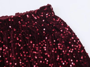 Close-up of wine red sequin fabric texture and elastic waistband details on velvet trousers