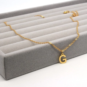 Detail of a gold stainless steel letter G pendant on a luxury velvet display tray