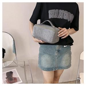 Detailed view of silver glitter makeup bag with top handle held by a model in casual attire