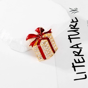 Detailed view of a gold-tone gift box brooch with red enamel bow and crystal accents