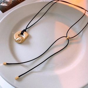 Close-up of golden irregular openwork pendant with adjustable black cord on ceramic tray