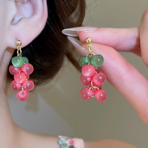 Detail of resin grape tassel earrings with pink beads and golden studs worn by model